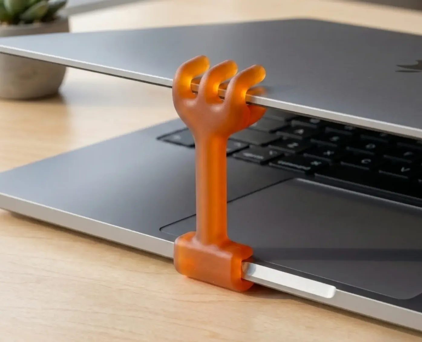 A small orange rubber hand propping a MacBook lid open a crack.